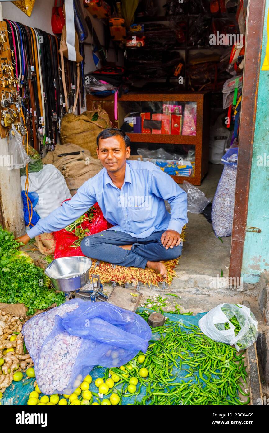 Shopkeeper sitting in the doorway of a small shop selling vegetables, street scene in Mahipalpur district, a suburb in New Delhi, India Stock Photo