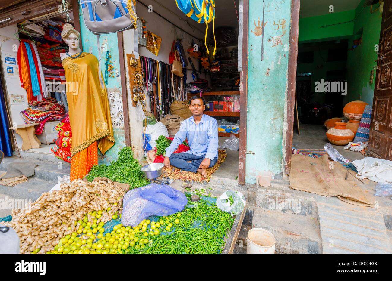 Shopkeeper sitting in the doorway of a small shop selling vegetables, street scene in Mahipalpur district, a suburb in New Delhi, India Stock Photo