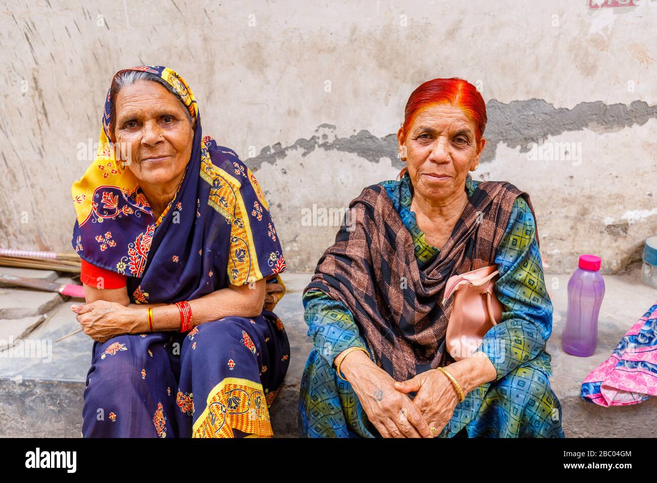 Street scene in Mahipalpur district, a suburb near Delhi Airport in New Delhi, capital city of India: old women sitting at the side of a street Stock Photo