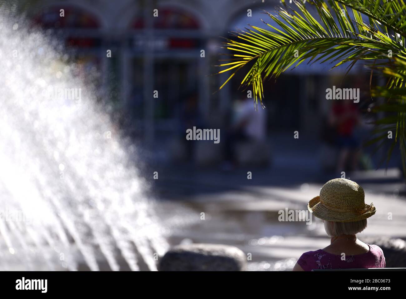 On a hot summer's day, a passer-by is looking for cooling at the edge of the Stachus fountain in downtown Munich. [automated translation] Stock Photo