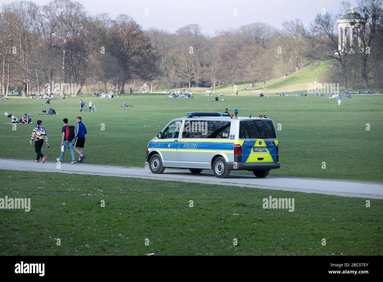 A police car drives through the English Garden on a mild spring day and warns those present by means of loudspeaker announcements to keep their distance in view of the danger of infection by the rampant corona virus. [automated translation] Stock Photo