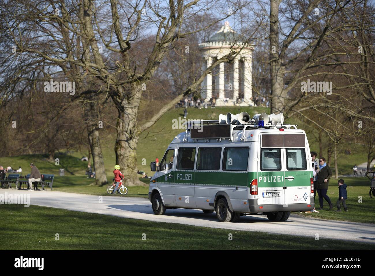 A police car drives through the English Garden on a mild spring day and warns those present of the danger of infection by the rampant corona virus by means of loudspeaker announcements. [automated translation] Stock Photo