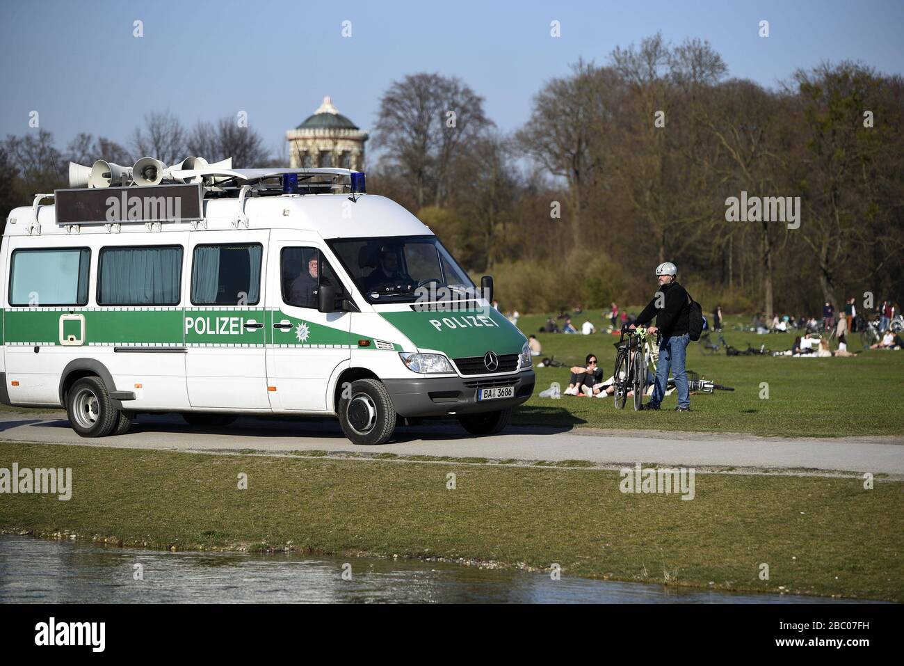 A police car drives through the English Garden on a mild spring day and warns those present of the danger of infection by the rampant corona virus by means of loudspeaker announcements. [automated translation] Stock Photo