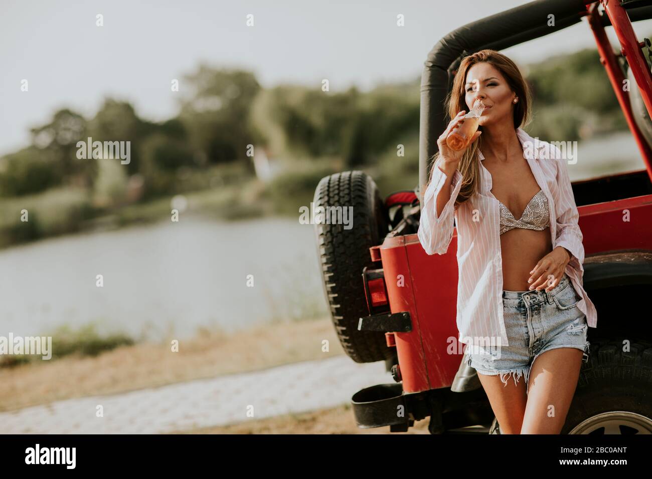 Pretty young woman relaxing by the car on the lakeside Stock Photo