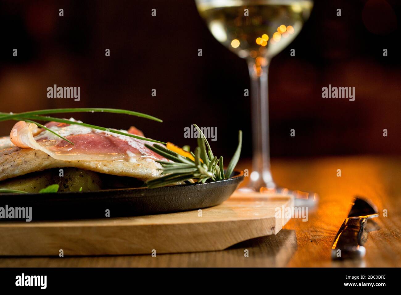 Sea bream stuffed with cream cheese and smoked ham with young potatoes and leek on the plate with glass of white wine Stock Photo