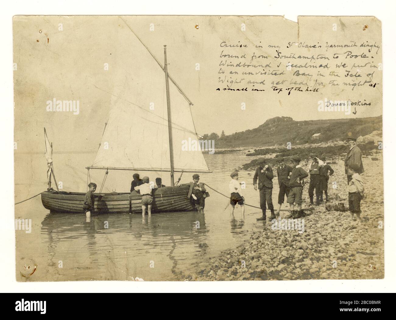 Original Edwardian era photo of charming tranquil coastal scene in early 1900's photo of a sailing cruise in St. Olave Yarmouth dinghy moored off a beach on Isle of Wight, small boys help whilst a man known as 'Dover Hoskins' looks on,  U.K. Stock Photo