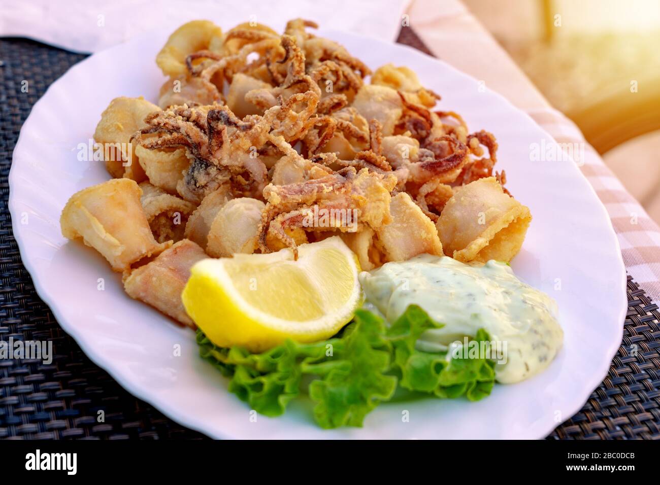 Deep fried calamari in an outdoor Restaurant in Croatia with tartare dip sauce and lemon Stock Photo
