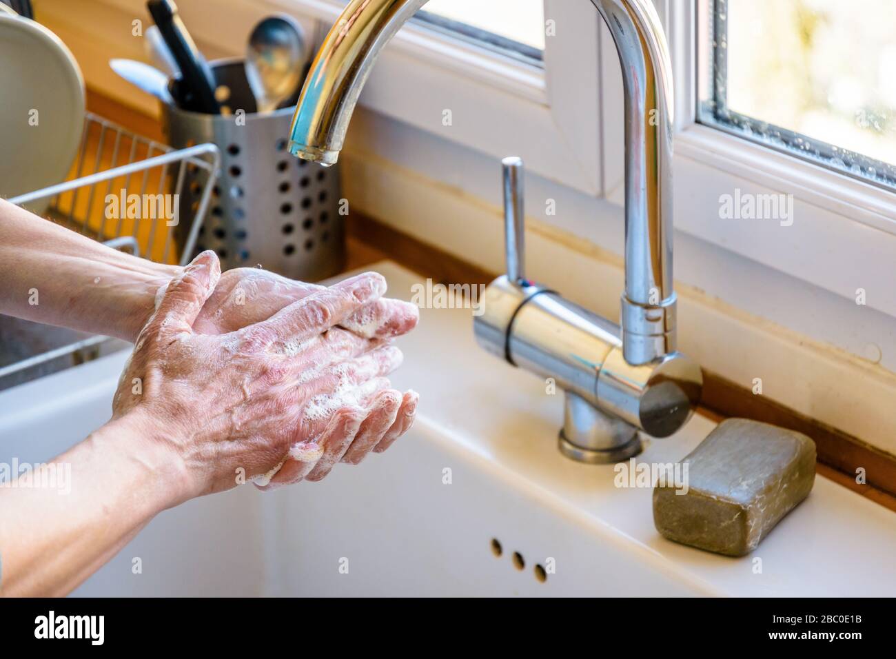 Close-up view on the hands of a woman washing her hands thoroughly with soap under the faucet of the kitchen sink. Stock Photo