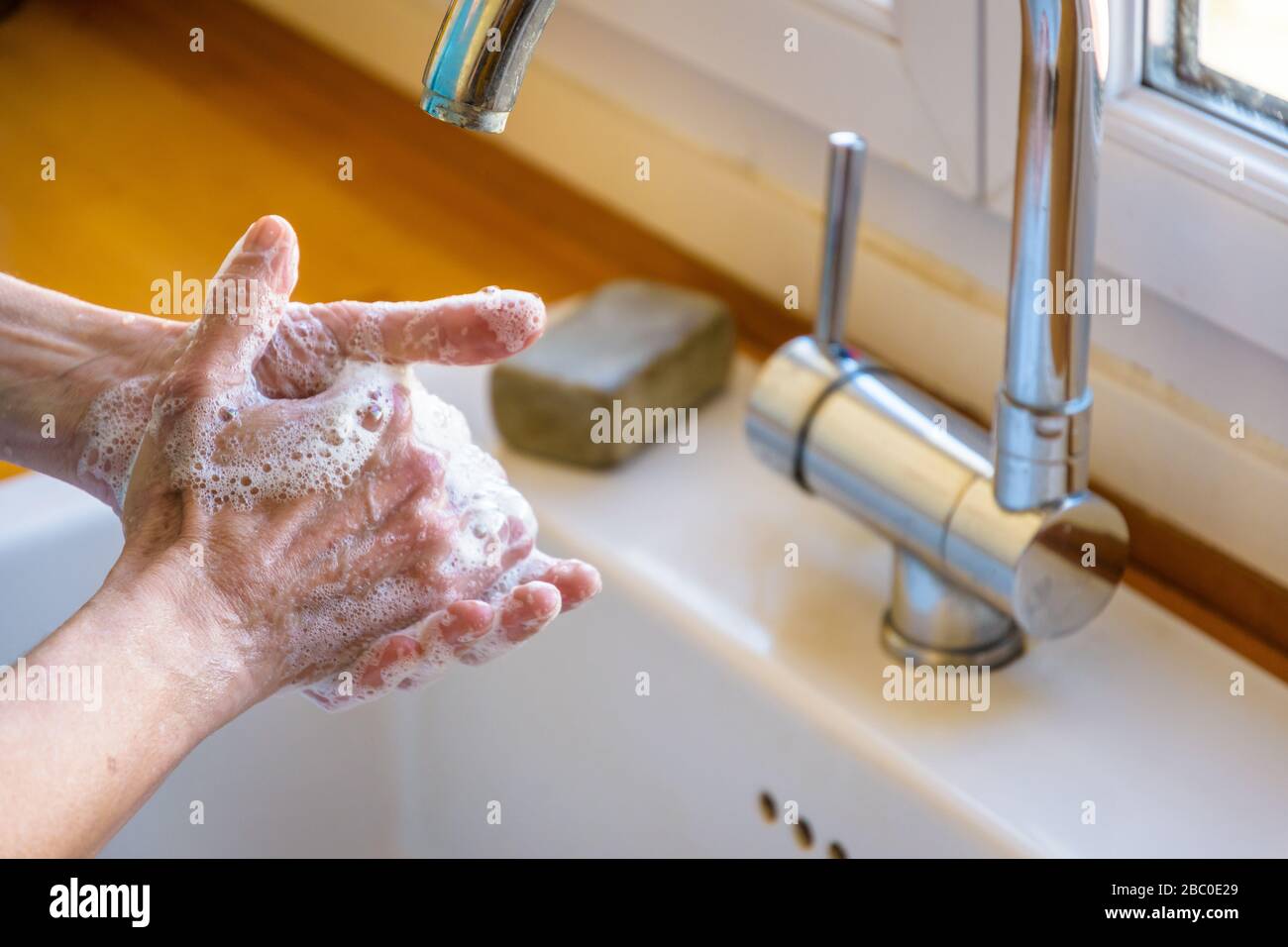 Close-up view on the hands of a woman washing her hands thoroughly with soap under the faucet of the kitchen sink. Stock Photo