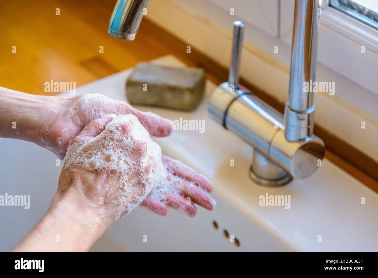 Close-up view on the hands of a woman washing her hands thoroughly with soap under the faucet of the kitchen sink. Stock Photo