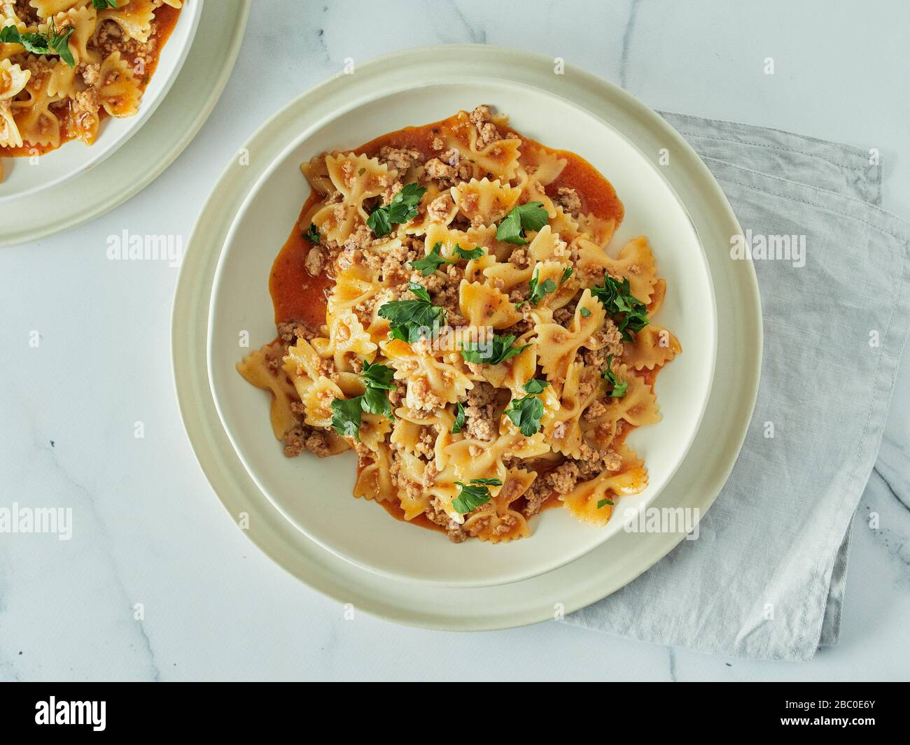 Pasta Farfalle with tomato sauce and ground meat in plate on white marble tabletop. Idea and recipes for easy, simple lunch or dinner one-pot meat goulash. Top down view or flat lay Stock Photo