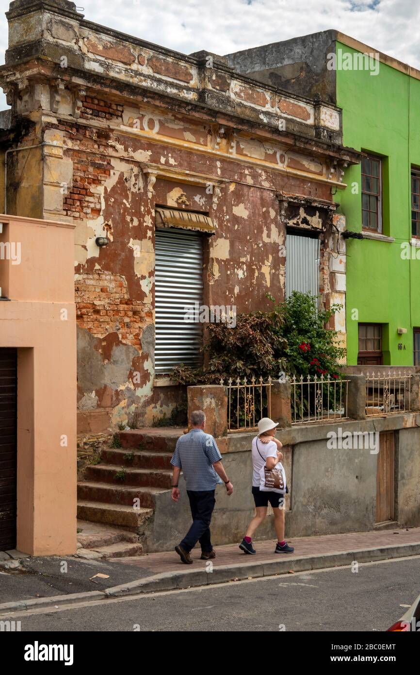 South Africa, Cape Town, Schotsche Knoof, Bo Kaap, Chiappini St, couple walking past unrestored building Stock Photo
