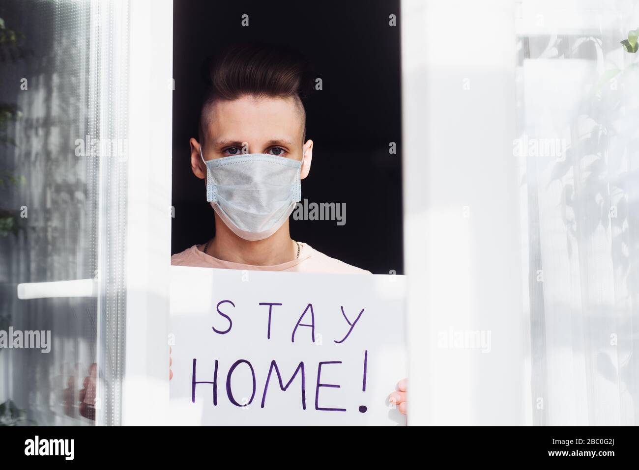 Young man in medical mask stay isolation at home for self quarantine. Concept home quarantine, prevention COVID-19, Coronavirus outbreak situation. Blank with the inscription: Stay at Home. Stock Photo
