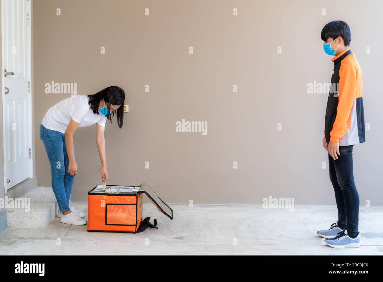 Asian woman unpacking and pick up delivery food bag from box and for contactless or contact free from delivery rider with bicycle in front house for s Stock Photo