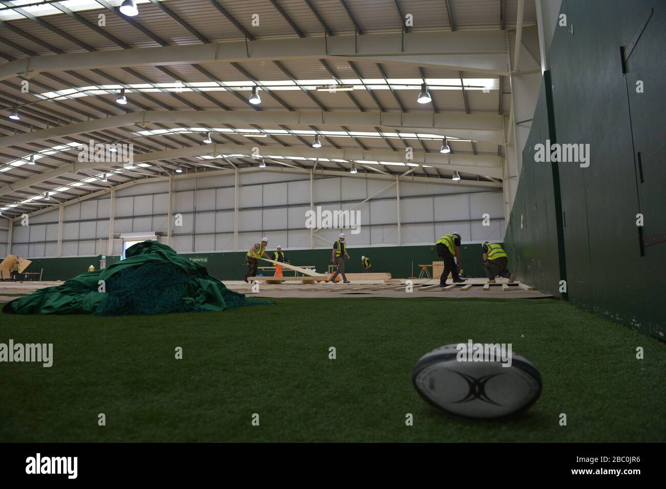 A discarded rugby ball and nets as workers lay flooring during the construction of a field hospital, which will hold up to 340 beds for coronavirus patients, at Llandarcy Academy of Sport, Neath, as the health services in the Swansea Bay area prepare their response to the coronavirus outbreak. Stock Photo