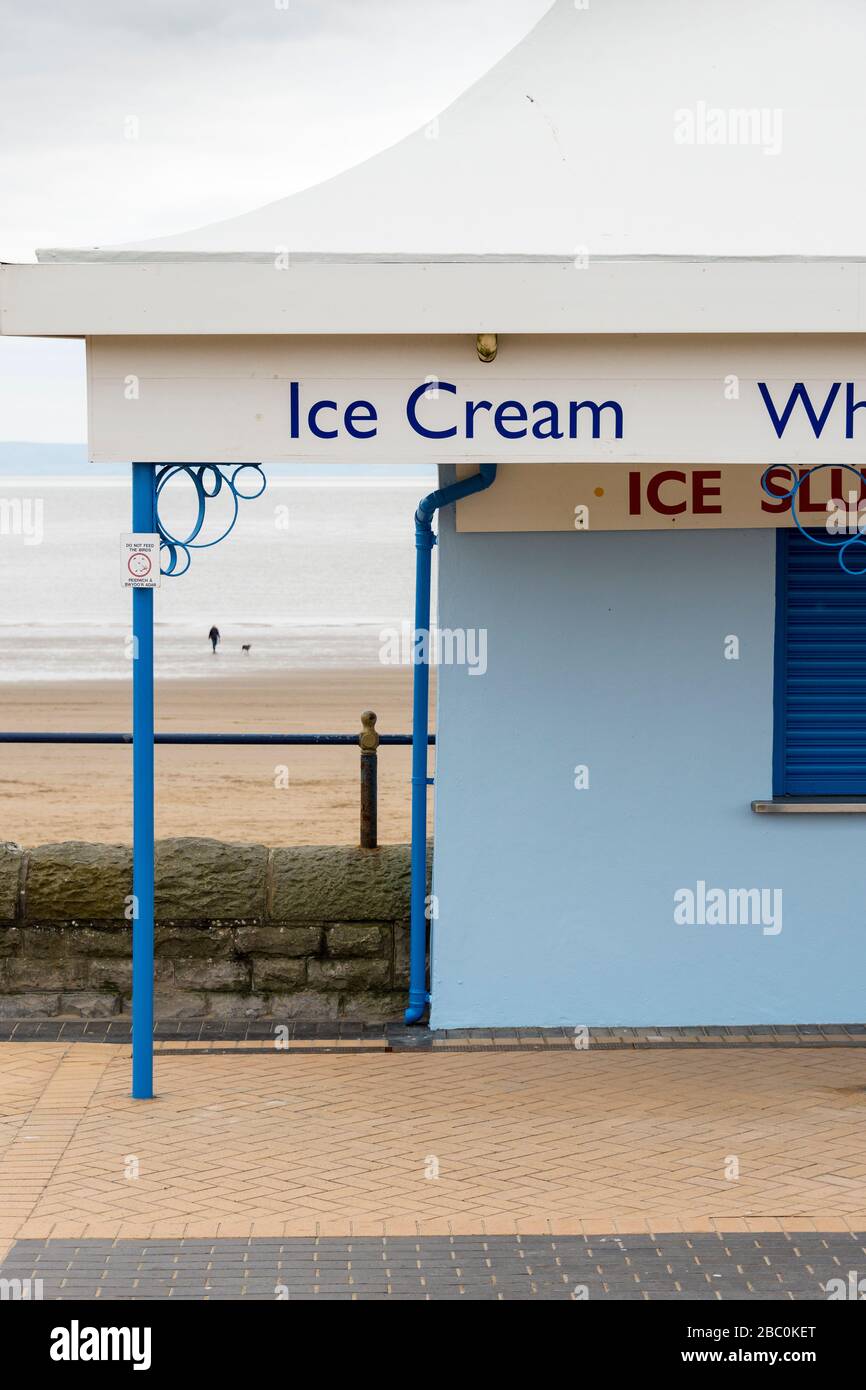 Partial view of closed café at Barry Island during the Covid-19 crises. A person and their dog can be seen in the distance on the beach. Stock Photo