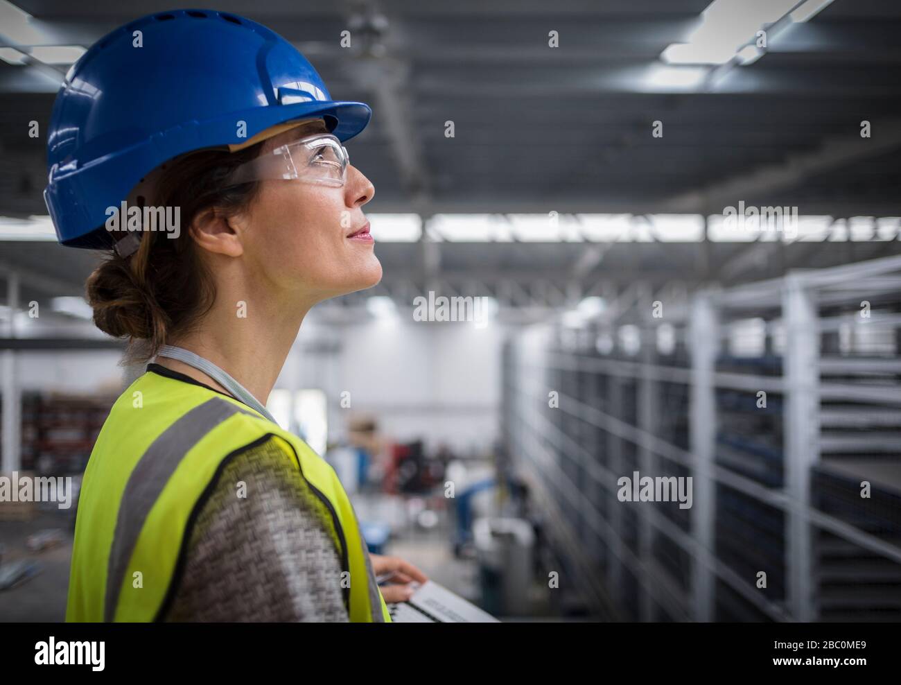 Smiling, confident female supervisor in hard-hat looking up in factory Stock Photo