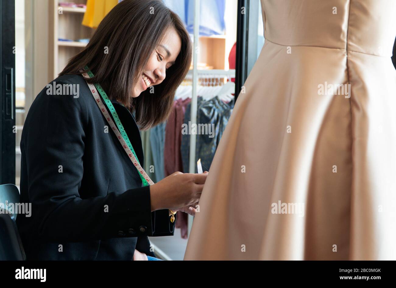Happy young Asian woman dressmaker fashion designer is checking for completion for a suit and Dress in a showroom. Concept of success young entreprene Stock Photo