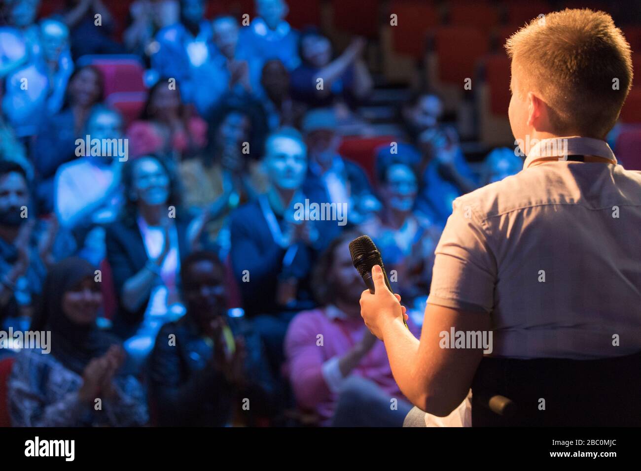 Female speaker in wheelchair with microphone on stage talking to audience Stock Photo