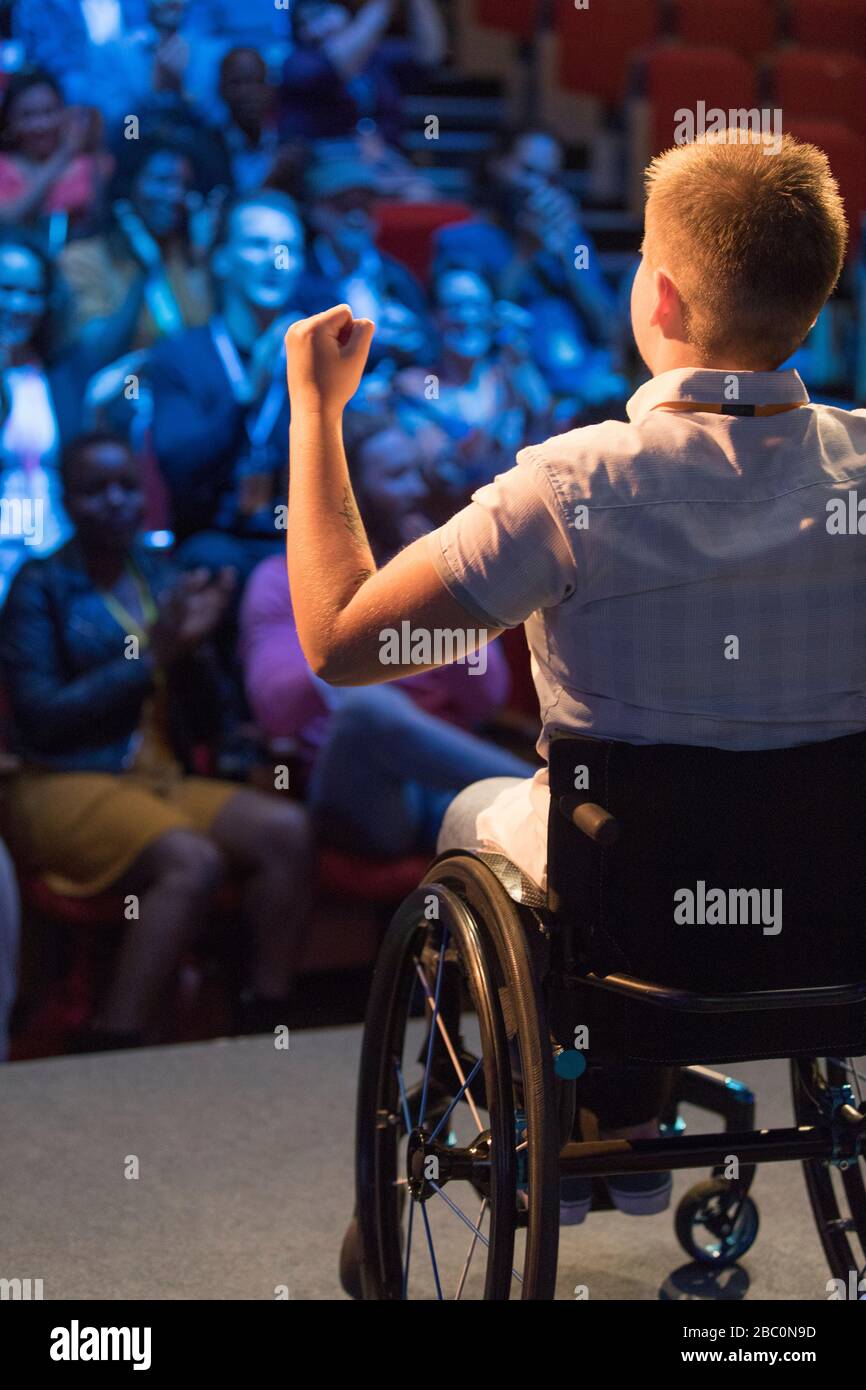 Female speaker in wheelchair gesturing on stage for cheering audience Stock Photo