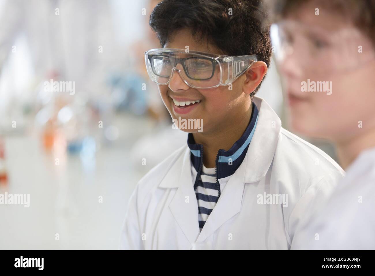 Smiling boy wearing goggles and lab coat in laboratory classroom Stock Photo