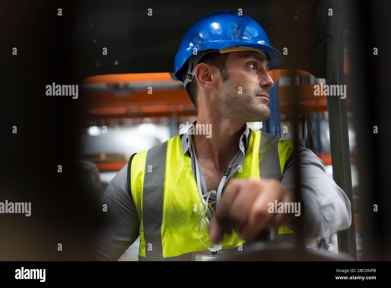 Male worker driving forklift, looking over shoulder in factory Stock Photo