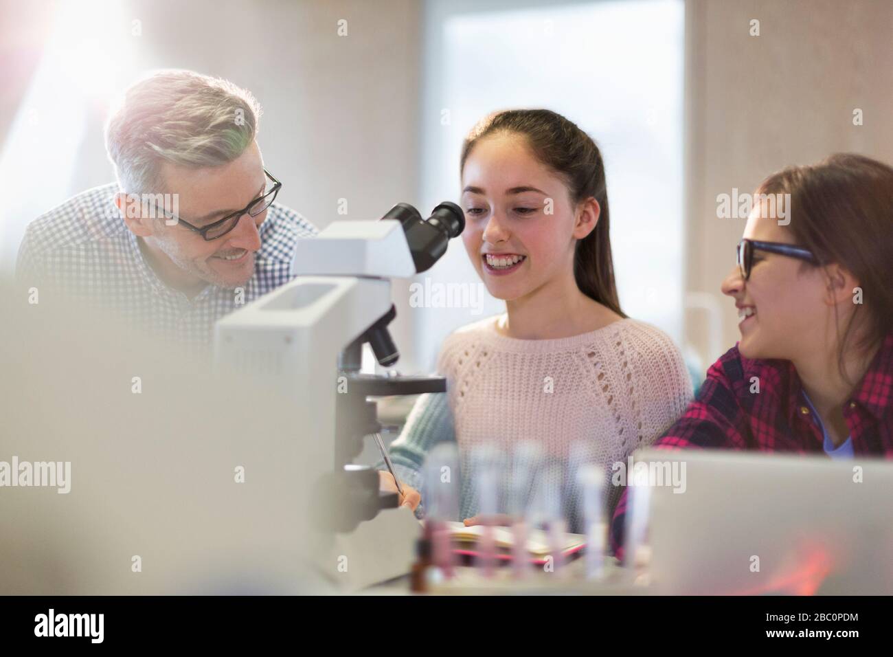 Male teacher and girl students conducting scientific experiment at microscope in laboratory classroom Stock Photo