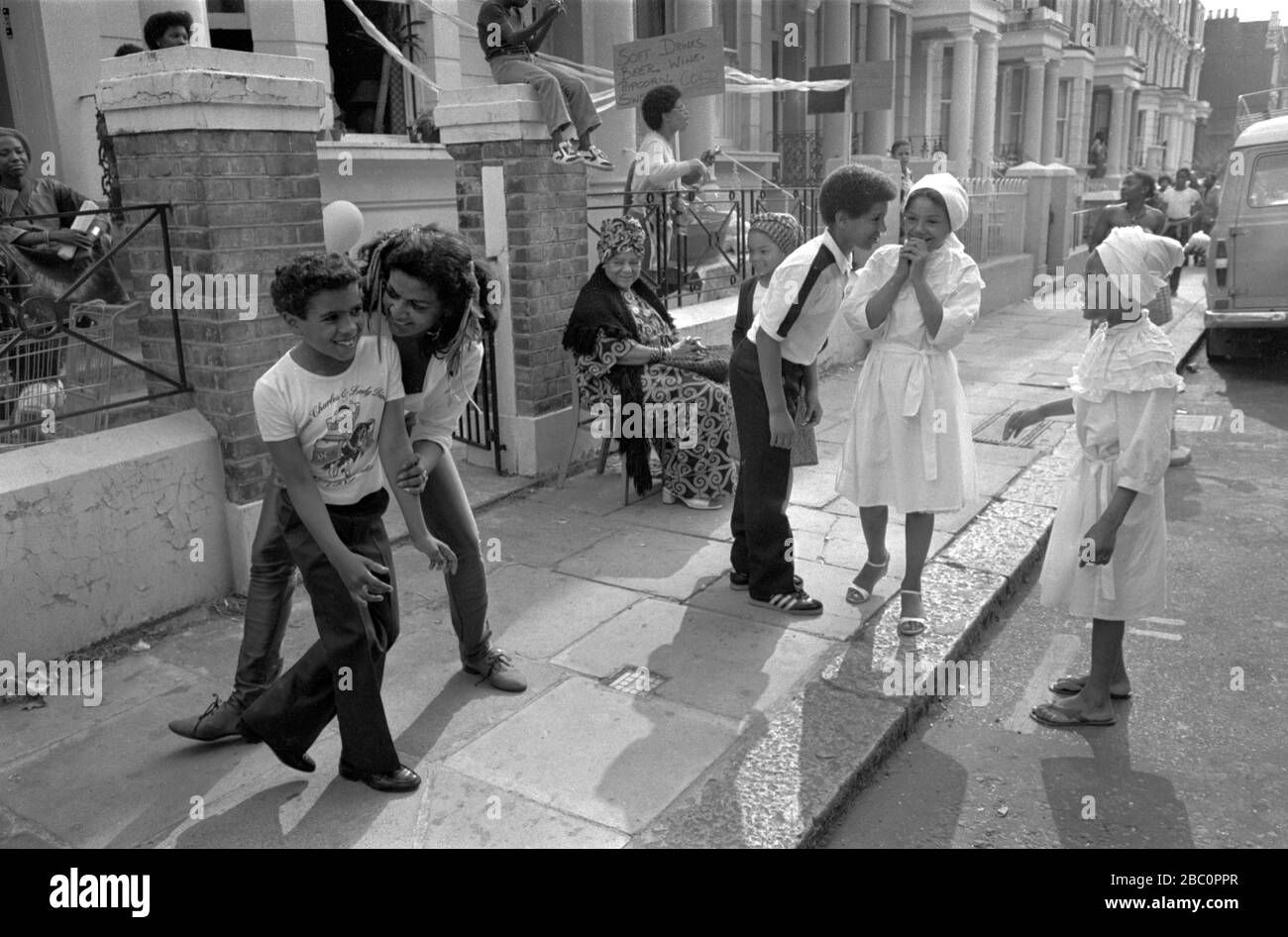 Notting Hill London 1980s UK An older woman with young kid being friendly, other children and adults watching having fun, laughing in the street .During the annual Notting Hill Carnival. 1980s England  HOMER SYKES Stock Photo