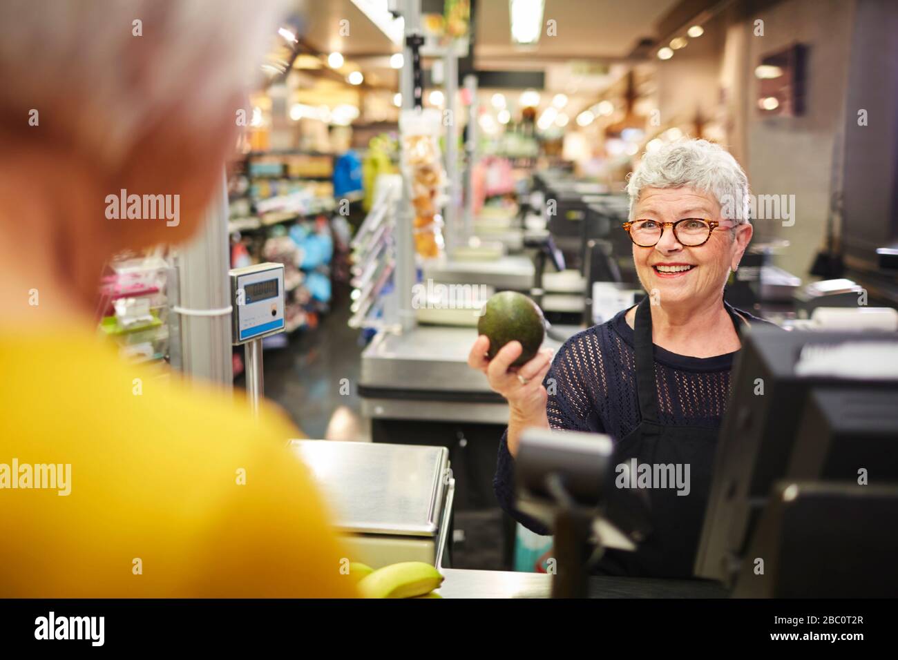 Smiling senior female cashier helping customer at grocery checkout Stock Photo