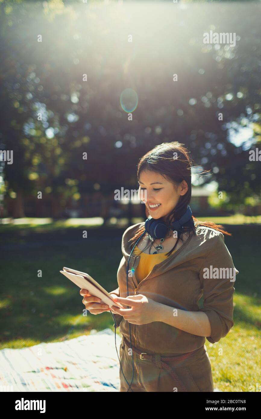 Smiling young woman with headphones using digital tablet in sunny summer park Stock Photo