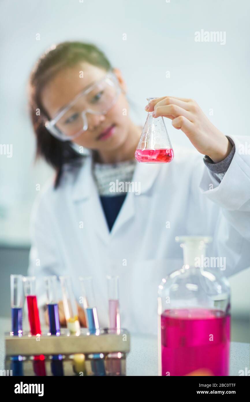 Girl student examining pink liquid, conducting scientific experiment in laboratory classroom Stock Photo