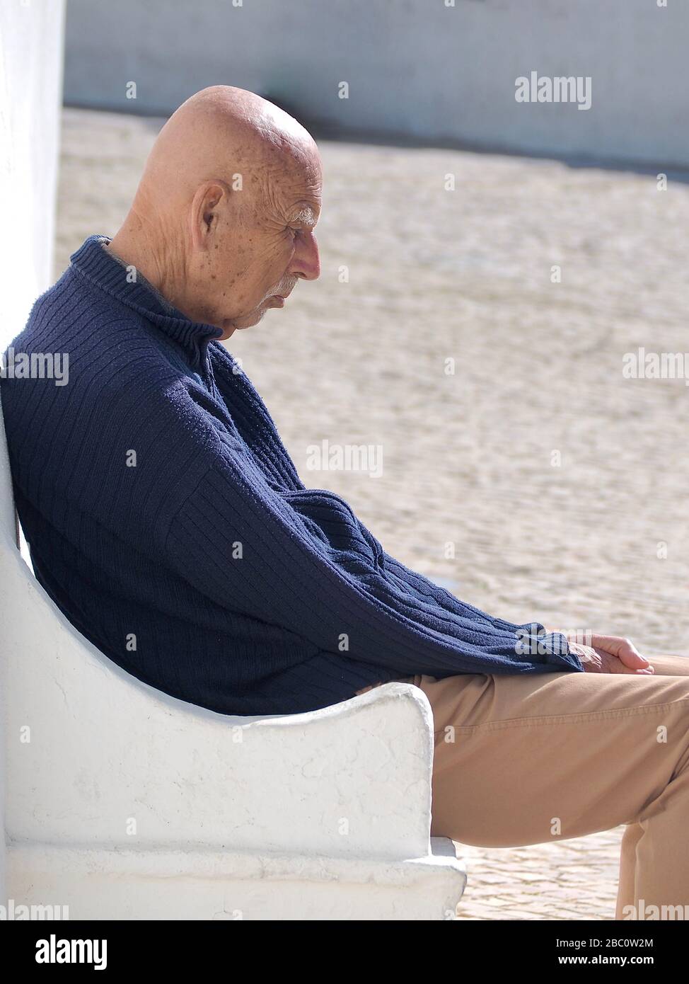 Single senior old man is sitting isolated outside with white background Stock Photo