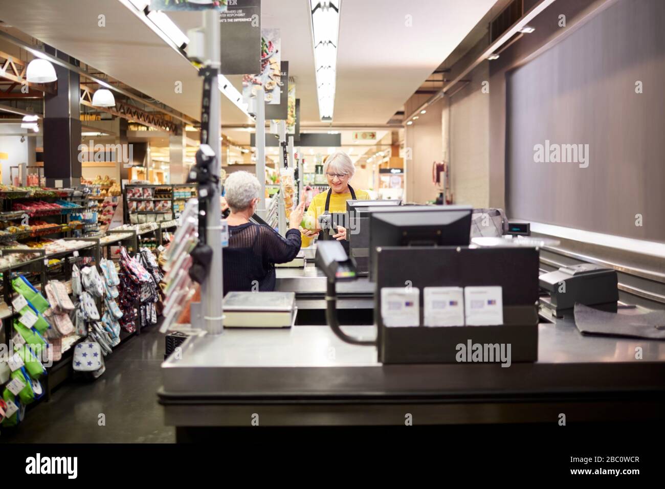 Senior female cashier helping customer at supermarket checkout Stock Photo
