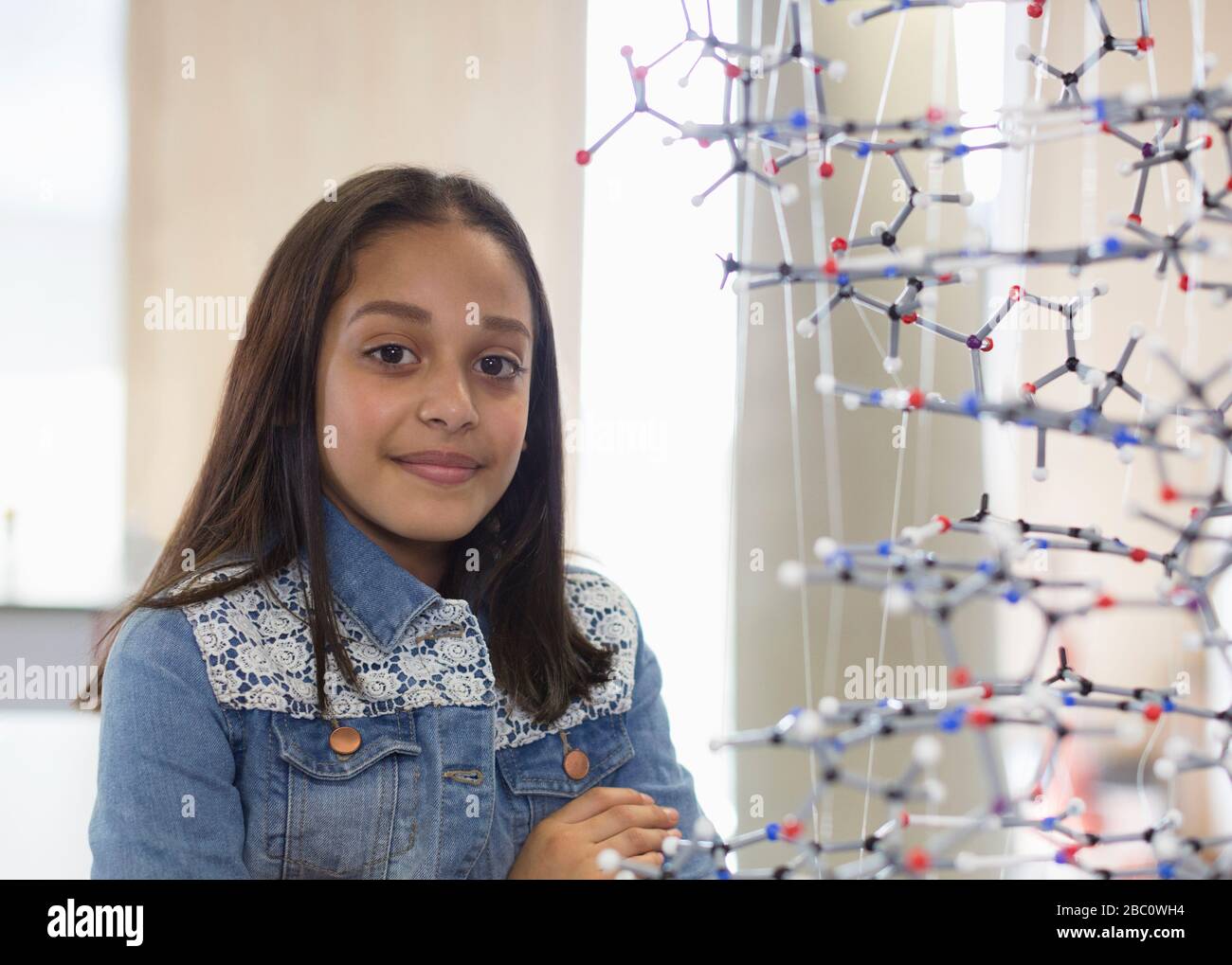 Portrait confident girl student next to molecular structure in classroom Stock Photo