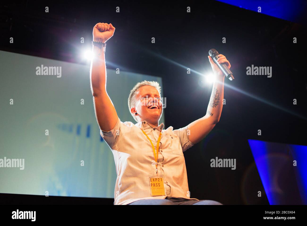 Enthusiastic, smiling female speaker with microphone cheering on stage Stock Photo