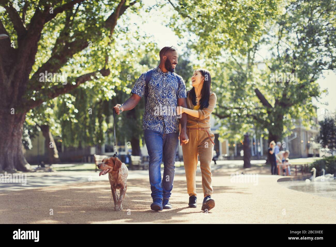 Happy young couple walking dog in sunny park Stock Photo