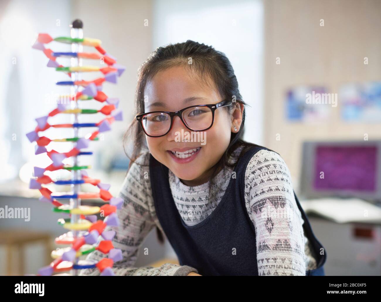 Portrait smiling, confident girl student next to DNA model in classroom Stock Photo