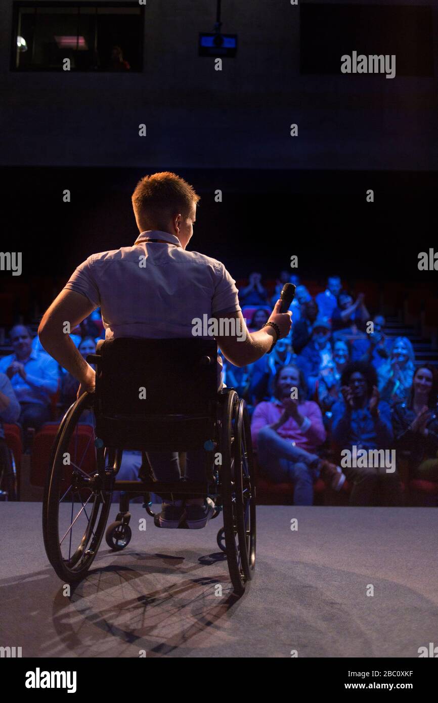 Female speaker with microphone in wheelchair on stage Stock Photo
