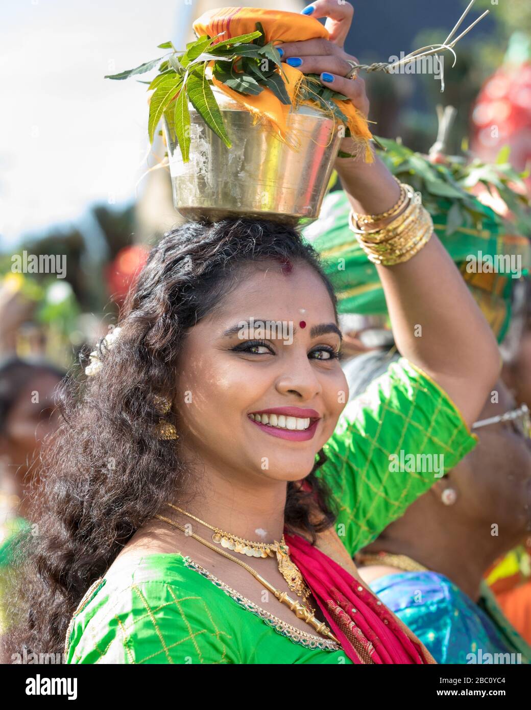 Young Hindu  in sari, smiling as she participates in a  Chariot Festival procession, carries offering on her head Stock Photo