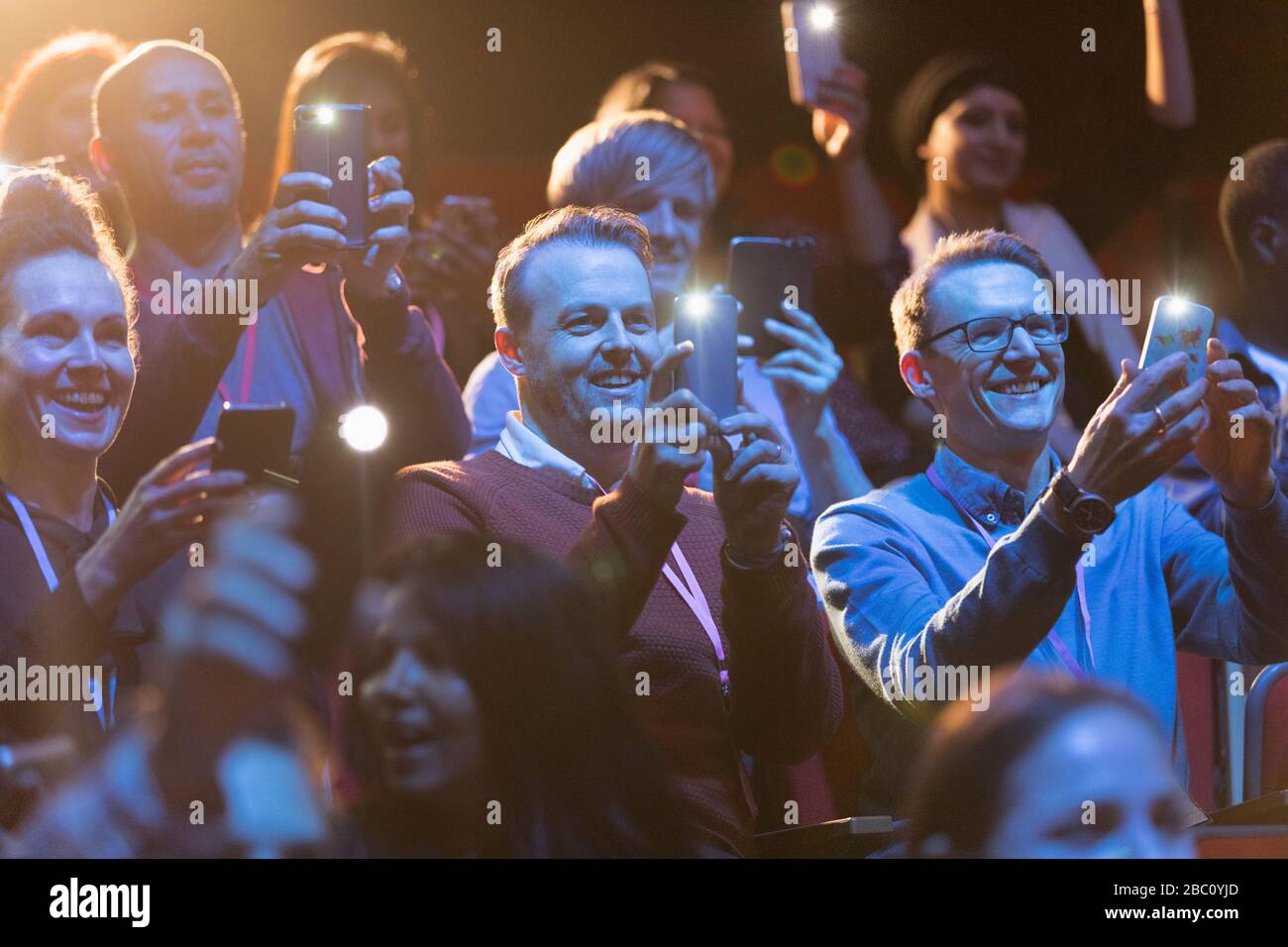 Smiling audience using smart phone flashlights Stock Photo