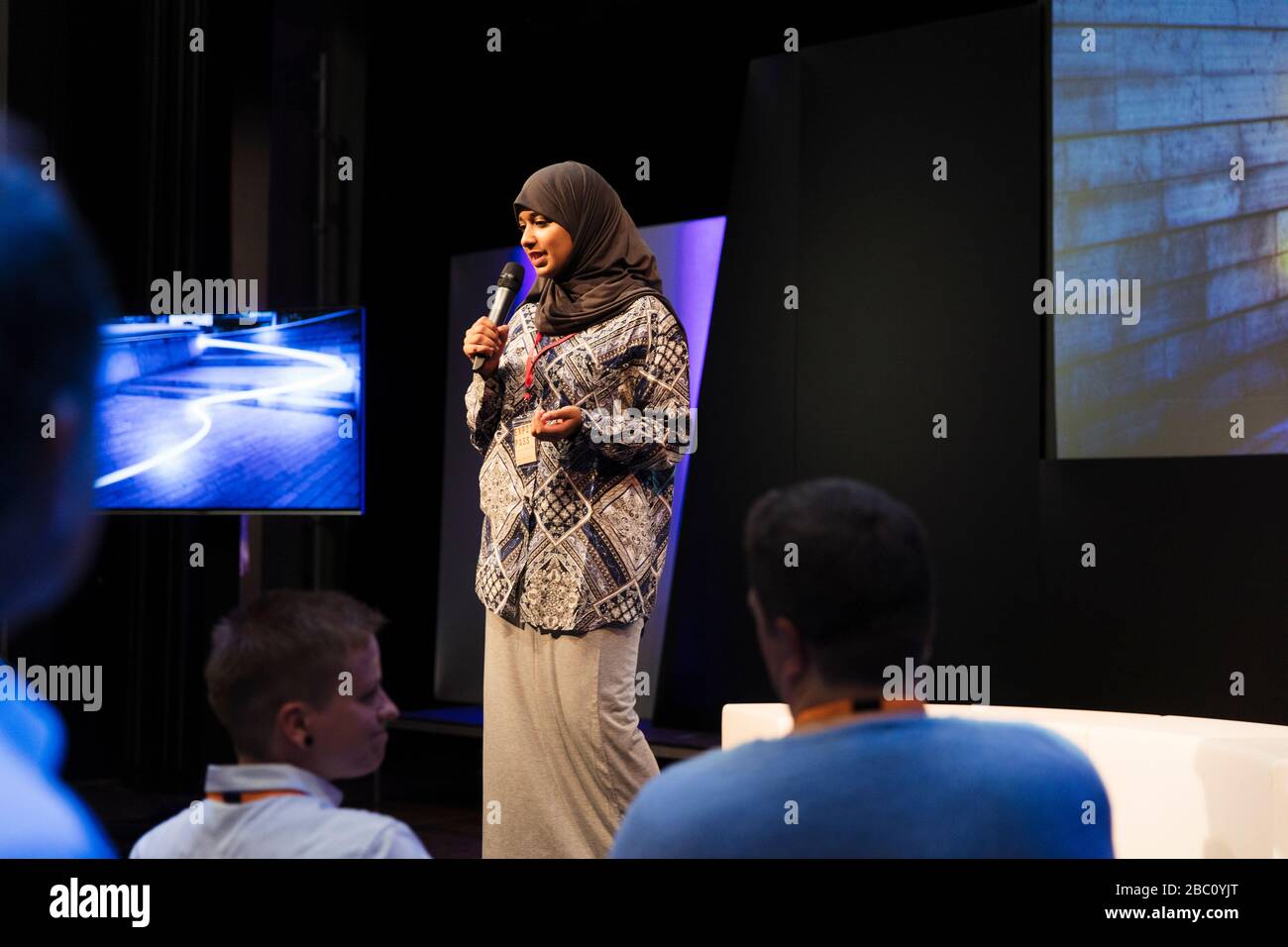 Female speaker in hijab on stage talking to audience Stock Photo