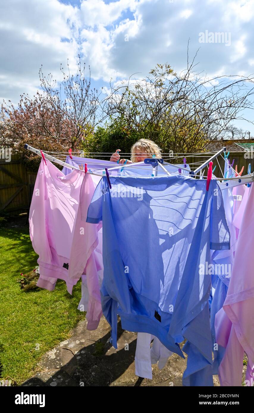 Woman hanging out various coloured mens shirts on a rotating washing line during in the wind in back garden UK Stock Photo