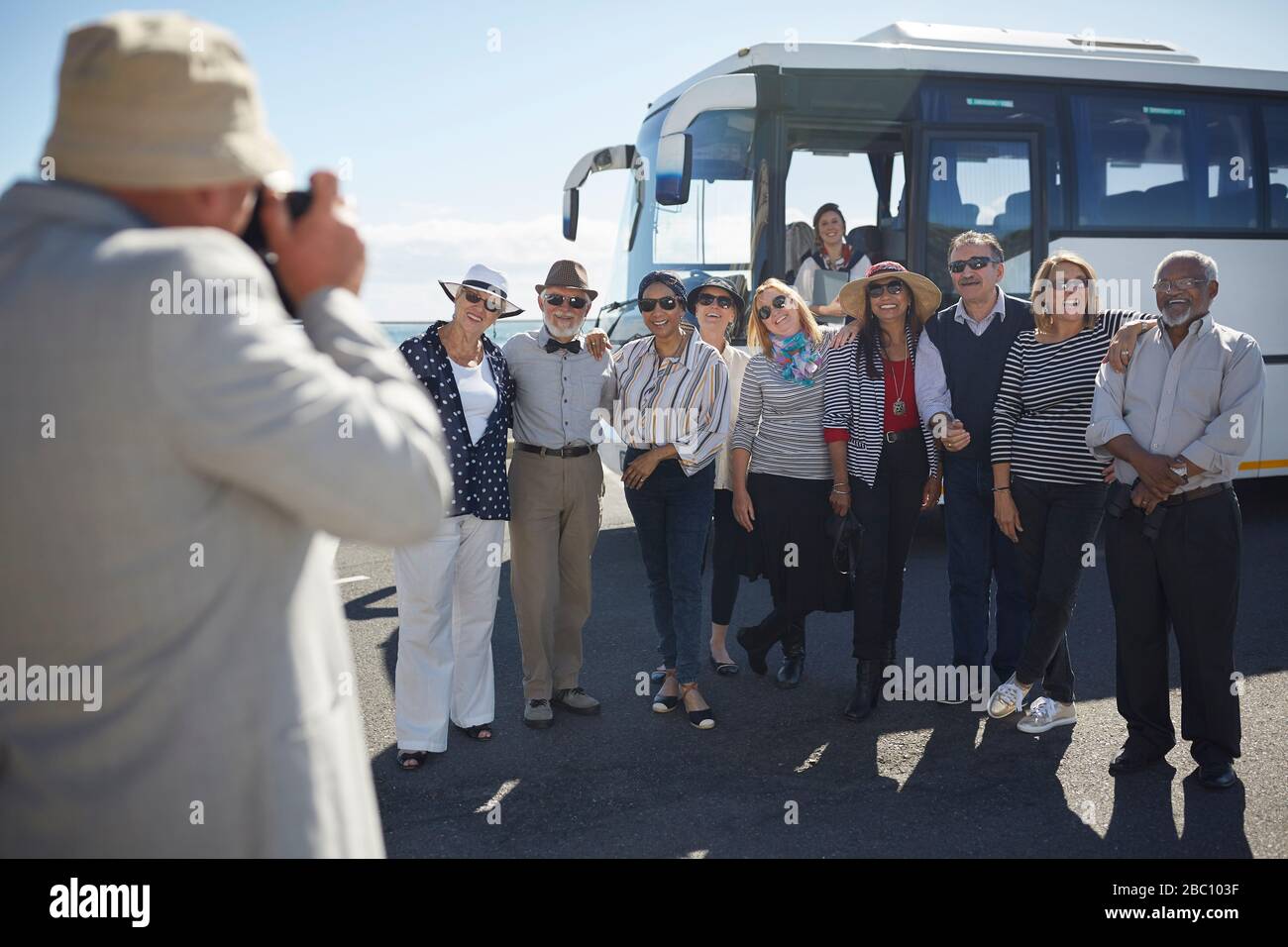 Active senior tourist friends posing for photograph outside tour bus