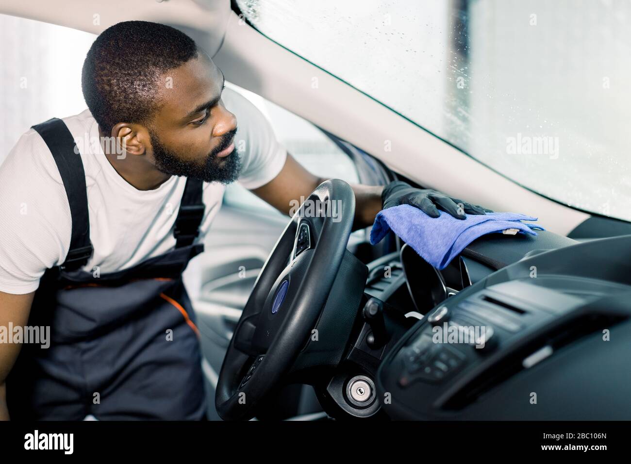 Concentrated professional African worker cleaning the car console and ...