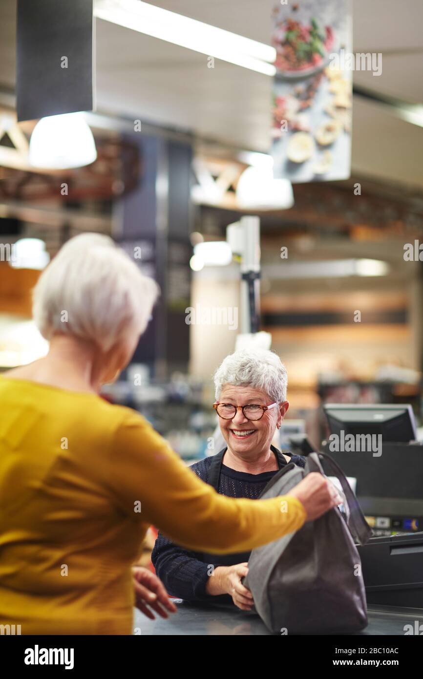 Friendly senior female cashier helping customer supermarket checkout Stock Photo