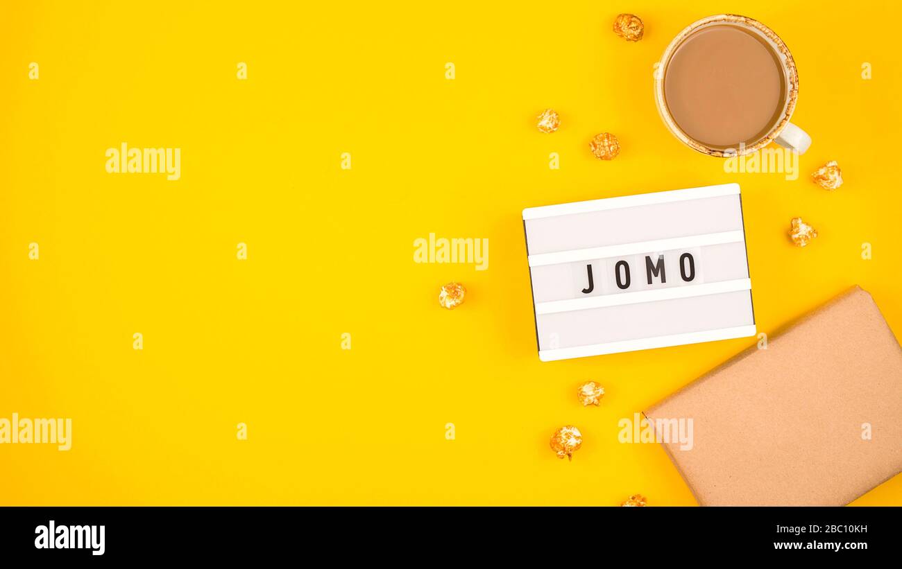 Abbreviation word JOMO written on a decorative board on a bright yellow background. The concept of relaxation from information and gadgets. Top view, flat lay, copy space. Stock Photo