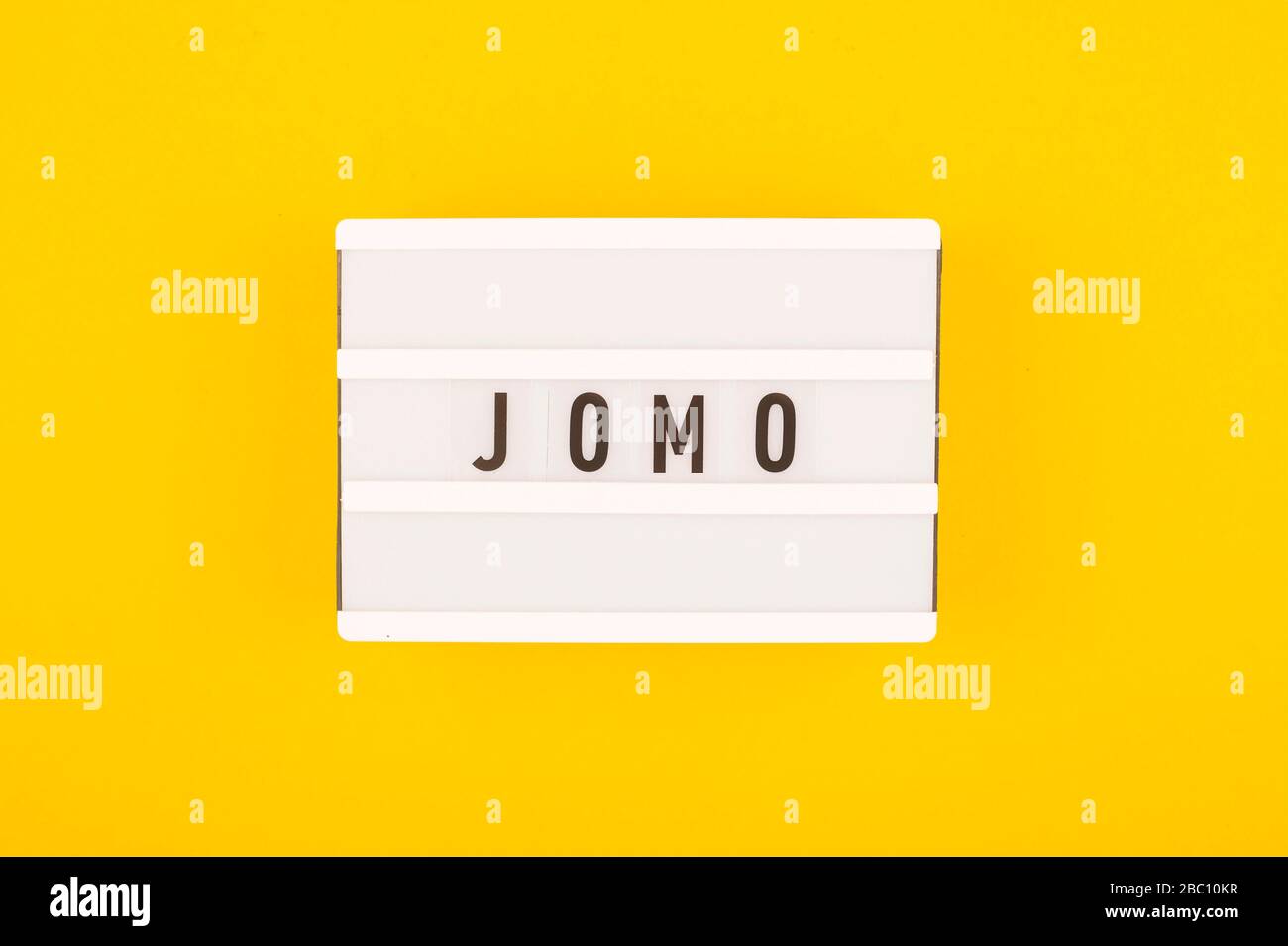 Abbreviation word JOMO written on a decorative board on a bright yellow background. The concept of relaxation from information and gadgets. Top view, flat lay. Stock Photo