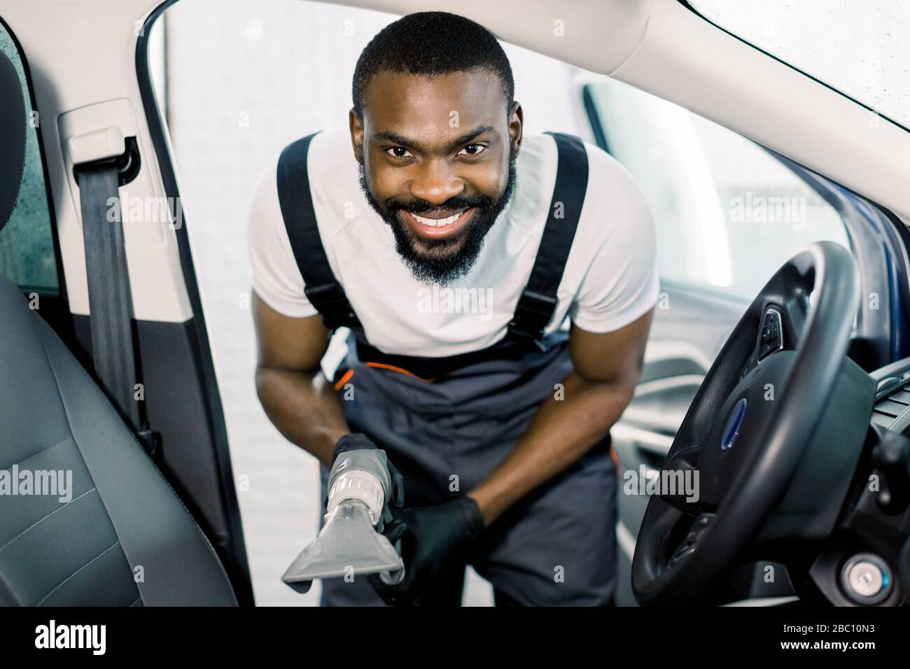 Young handsome African man cleaning car front seat with wet vacuum