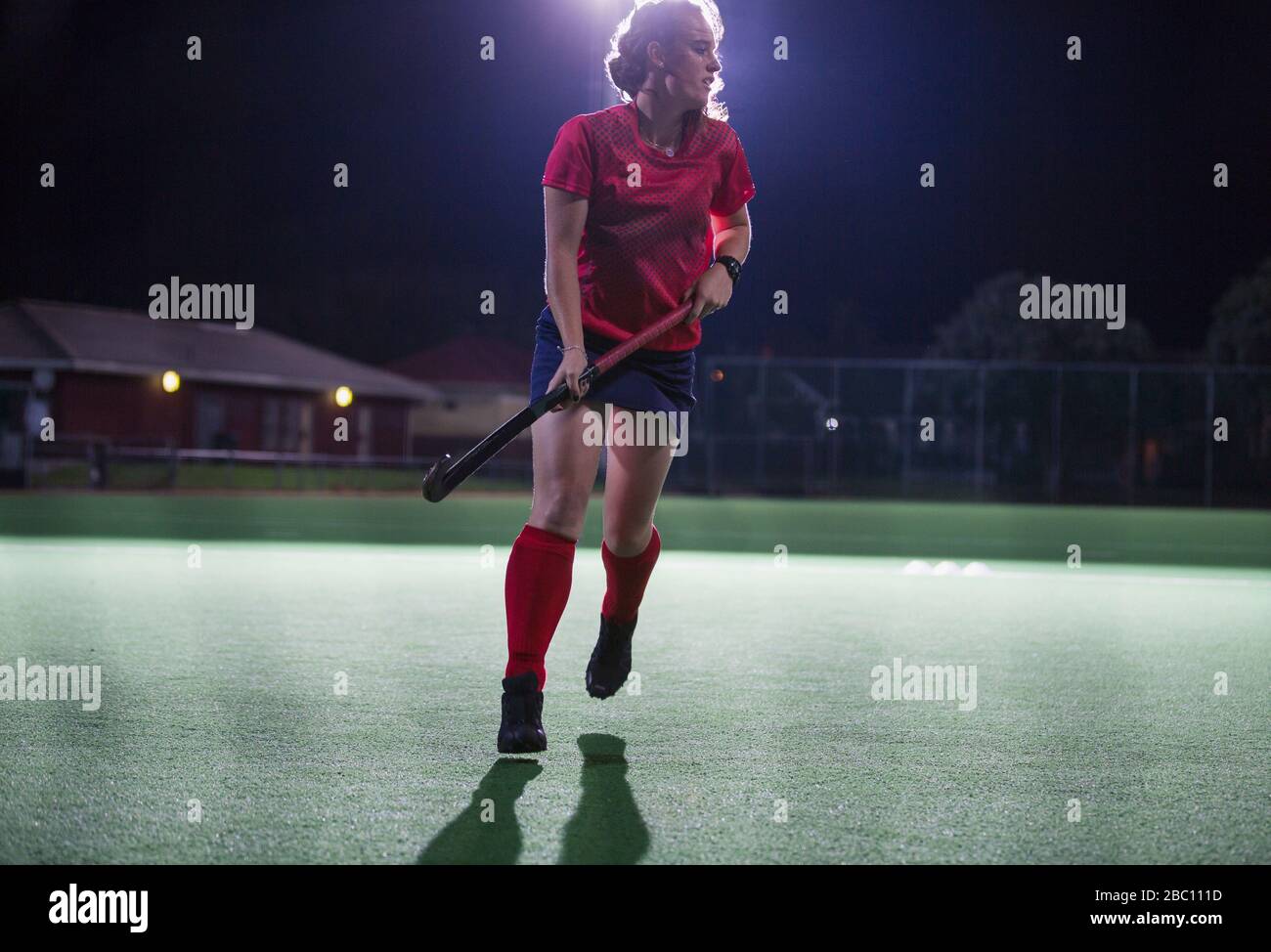 Young female field hockey player running with hockey stick on field at night Stock Photo