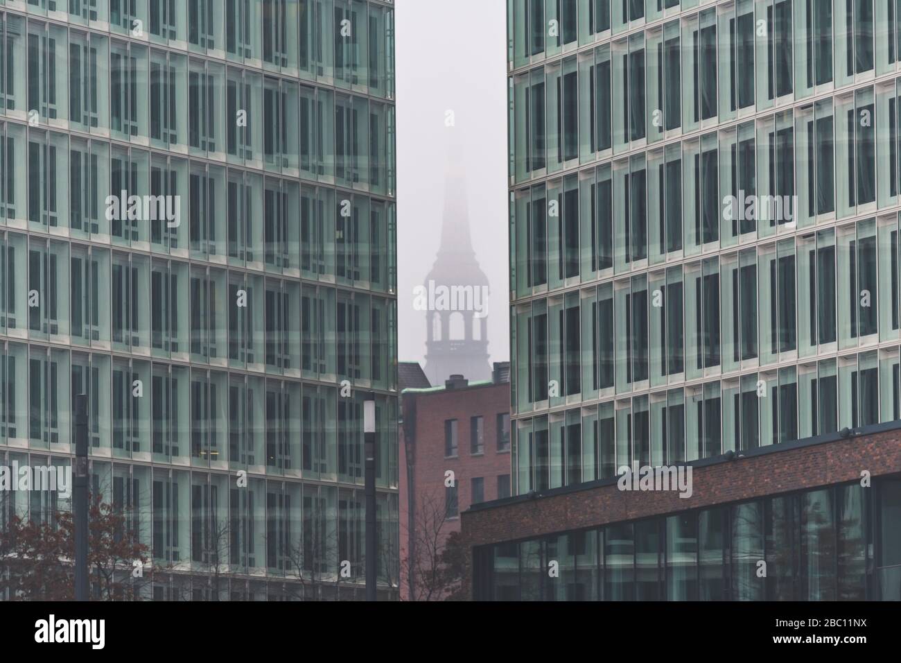 Germany, Hamburg, Fog shrouding tower of Saint Catherines Church seen between Ericusspitze buildings Stock Photo